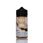 A 100ml bottle of Kilo Vanilla Almond Custard e-liquid on a white background with a reflection below. The bottle has a black cap and a label featuring brown and beige tones with vanilla and almond imagery.