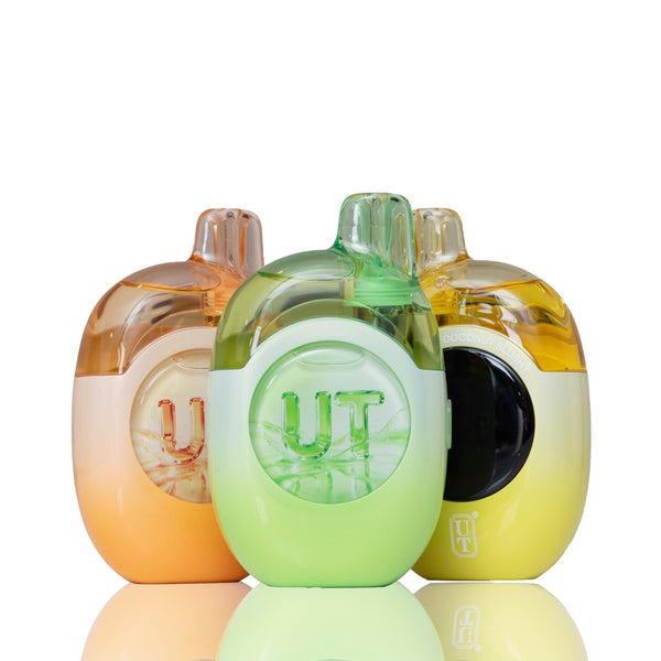 Three small translucent vape devices with rounded bodies and mouthpieces, arranged together on a white reflective surface. The center device is light green with a clear front showing the word "UT" and a black circular side detail.